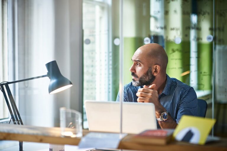 Mature man at desk looking off in thought ZmWPIf1