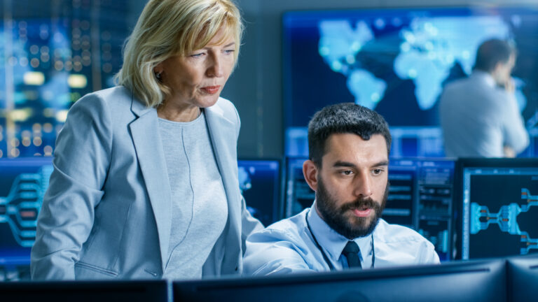 two people in an office looking at a computer monitor and discussing what is on it