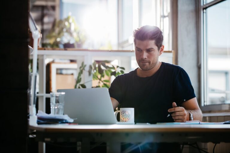 young man sitting at desk using laptop and thinking LfWdYQh