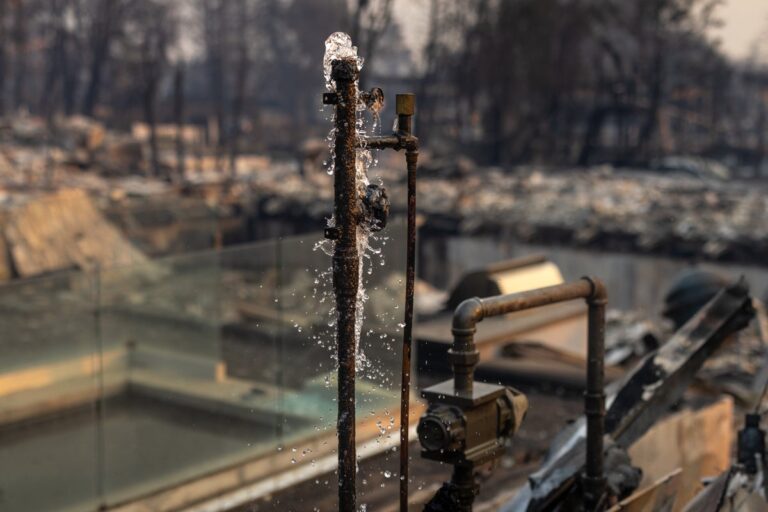 Water runs from a pipe of a destroyed home